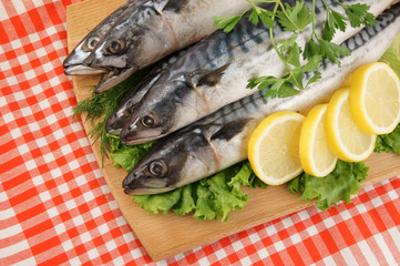 Mackerel fish with greens, lemon and cutting board on tablecloth