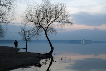 Silhouette of loving couple on the beach against the background of a sunset over the lake.