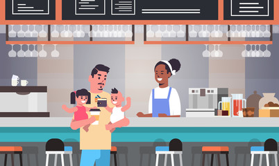 father with little son and daughter at cafe counter paying for coffee fatherhood concept happy family having fun modern cafeteria interior flat portrait horizontal