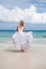 Fototapeta na wymiar young beautiful woman in a long white bride dress runs along the edge of the blue sea