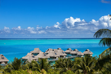 Blue lagoon of the Bora Bora island, Polynesia. Top view on palm trees, traditional lodges over water and the sea