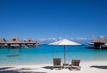 Fototapeta na wymiar beach chairs and sun umbrella on the beach and houses over the sea. Tahiti