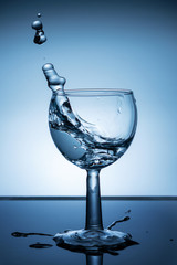 Splash of water in a wine glass on dark blue background. Close up.