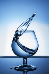 Splash of water in a glass on dark blue background. Close up.