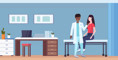 african american doctor examining woman patient by stethoscope checking heart beat or breath medicine healthcare concept modern hospital office interior full length horizontal