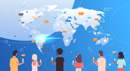rear view people using mobile messenger application men women holding smartphones sending email envelope letter global communication concept world map background flat portrait horizontal © mast3r
