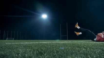 American football ball is getting caught by a player on a field at night