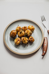 A vertical photo of baked baby potatoes with salt, pepper, olive oil and thyme. Natural light, white background, blue plate, fork and knife.