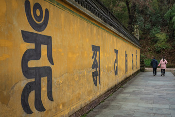 Fototapeta premium Great Buddha temple area, Xinchang, China - January 6, 2019 : Visitors of the temple complex walking past a long wall with inscriptions