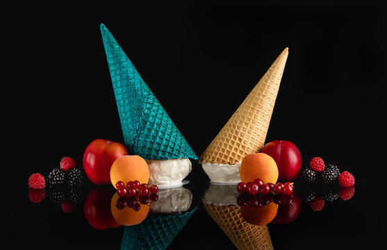 Composition of BlackBerry , red currant, red plum , apricot, raspberry. In the center with colorful waffle cones with ice cream. On a dark background with reflection.