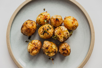 A photo of baked baby potatoes with salt, pepper, olive oil and thyme. Natural light, white background, blue plate. Top view.