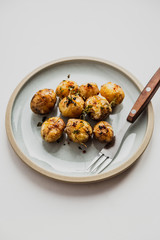 A photo of baked baby potatoes with salt, pepper, olive oil and thyme. Natural light, white background, blue plate, fork.