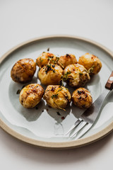A photo of baked baby potatoes with salt, pepper, olive oil and thyme. Natural light, white background, blue plate, fork.