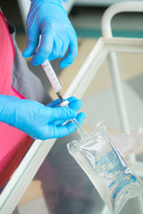 Close-up hands of young woman doctor anesthesiologist dressed in pink gown, blue gloves prepares solution for anesthesia in the operating room before the surgery.