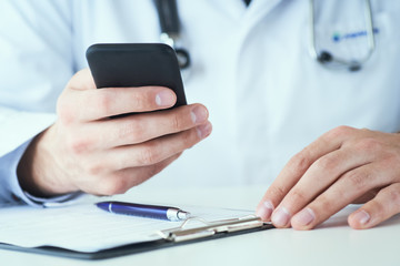 Fototapeta premium Male doctor in white coat is using a modern smartphone device with touch screen. Male doctor hands with mobile phone close-up.