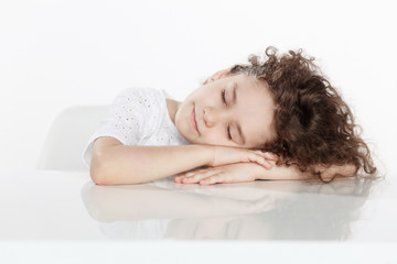 Obraz na płótnie Canvas Adorable little curly girl sleeping paceful on a table, isolated on a white background. Horizontal view.
