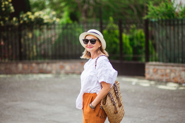 Happy blonde mature woman in hat and sunglusses walking outdoor sliming. Senior woman relaxing in a summer day. © Anna