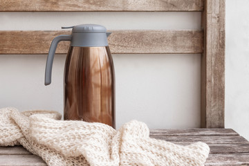 Big thermos on the wooden bench with scarf. Horizontal