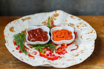 Red pepper, pomegranate seeds, parsley leaf on fried pita bread. The substrate for delicious grilled meat. Meat sauces, ketchup, Armenian Aivar. Horizontal close-up photo.