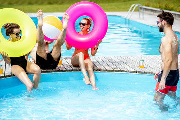 Group of a happy friends having fun, playing with inflatable balls and rings on the water pool outdoors during the summer time