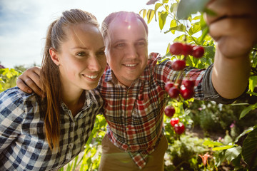 Young and happy farmer's couple at their garden in sunny day. Man and woman engaged in the cultivation of eco friendly products. Concept of farming, agriculture, healthy lifestyle, family occupation.
