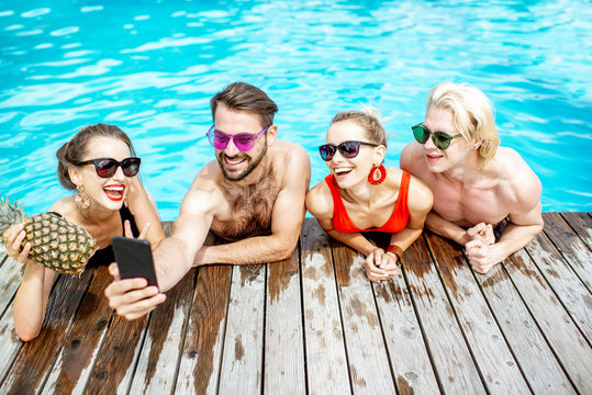 Group of a happy friends making selfie photo with phone, while having fun on the swimming pool outdoors during the summertime