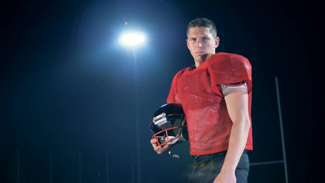 Male American football player player is standing with his helmet at the stadium at night