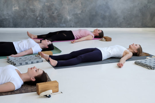 Group of young sporty women practicing yoga lesson, doing Dead Body, Savasana, exercise Corpse pose. Well being, health and relax concept