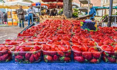 Close up fresh red strawberry berries in plastic containers in wooden box on retail display of farmers market, high angle view