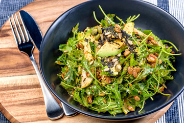 A fresh pear and avocado salad in a blue bowl, knife and fork on a blue place mat.