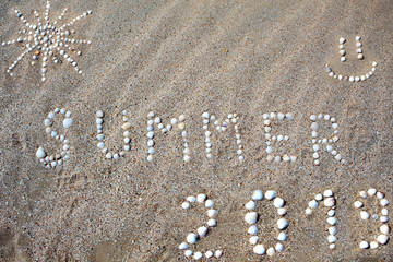 The word summer, the figure of the sun and the smile, the figure 2019 are laid out on the sand with shells. There is free space, space for text. Background.