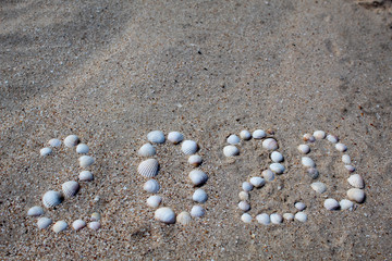The figure "2020" is laid out on sand with shells. There is free space, space for text.