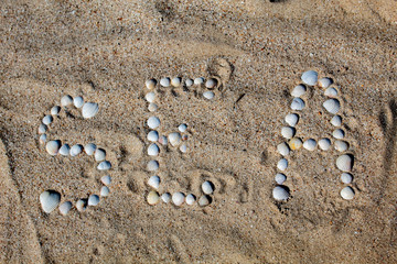 Fototapeta na wymiar The word sea in English, laid out on the sand with shells. There is free space, space for text. Background.