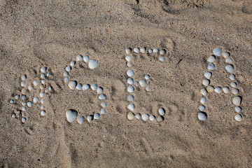The word sea in English, laid out on the sand with shells. There is free space, space for text. Background.