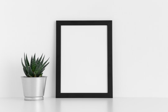 Black frame mockup with a cactus in a pot on a white table. Portrait orientation.
