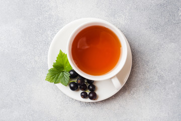 Cup of tea and fresh blackcurrant berries on grey table. Copy space.