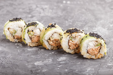 Japanese maki sushi rolls with tuna, cucumber, black sesame, cheese, on black concrete background. Side view.