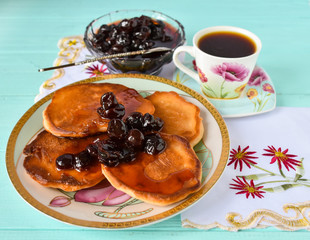 Plate with pancakes, cherry jam and two cups of coffee on a wooden blue table.