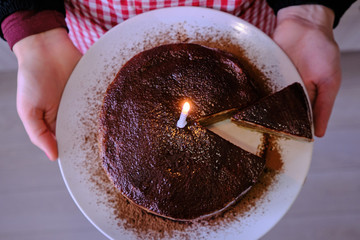Woman holding a chocolate cake. Girl's hand with a plate on which lay the cakes. A lighted candle on a birthday cake for one year. The view from the top.