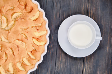 Fruit cakes in a baking dish. Homemade pie of ripe apples on a wooden dark background. Large apple pie and cup of milk.