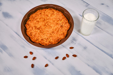 Cake from nuts in form for baking and a cup milk. Pie with almond on a wooden white background. Cakes made with almond flour and nuts lying.