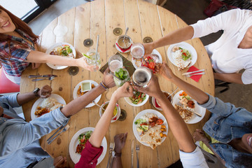 leisure, food and people concept - group of happy international friends eating and clinking glasses at restaurant table