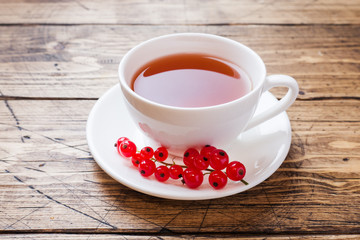 Cup of tea and fresh red currant berries on wooden table. Copy space.