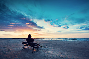 Man in hood sitting on a lonely bench on the beach
