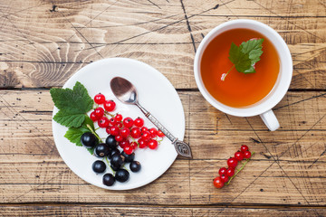 Cup of tea and fresh black and red currant berries on wooden table. Copy space.