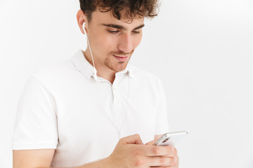 Photo closeup of young curly man in casual t-shirt using earphones and holding smartphone