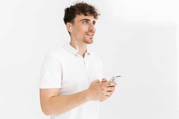 Photo closeup of caucasian curly man in casual t-shirt smiling while using earphones and holding smartphone