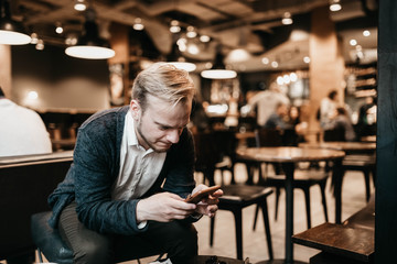 european male businessman with glasses uses a smartphone in a coworking cafe with a warm cozy light