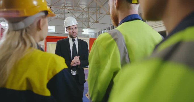 Portrait of young factory manager talking to group of workers