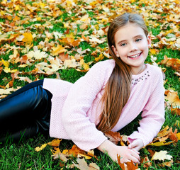 Autumn portrait of adorable smiling  little girl child lying on grass with leaves